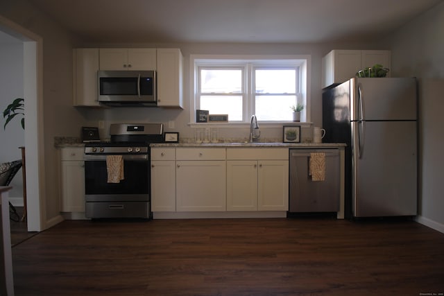 kitchen with sink, appliances with stainless steel finishes, white cabinetry, dark hardwood / wood-style floors, and light stone counters