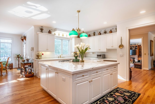 kitchen with a kitchen island, white cabinets, hanging light fixtures, ornamental molding, and a healthy amount of sunlight