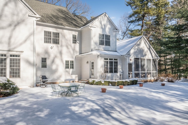 snow covered back of property with a sunroom