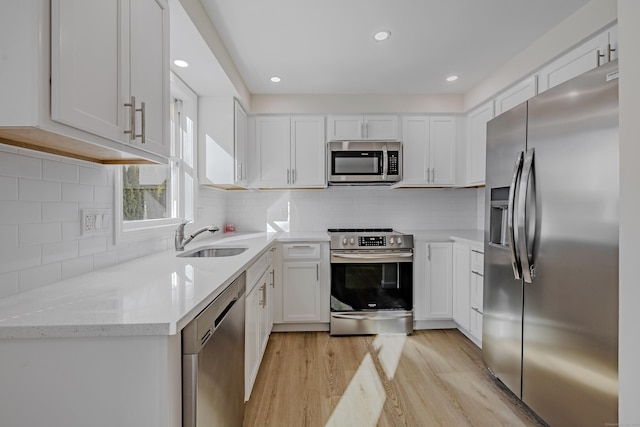 kitchen featuring sink, white cabinetry, light hardwood / wood-style flooring, appliances with stainless steel finishes, and light stone countertops