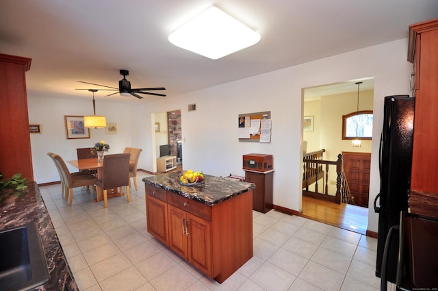 kitchen with light tile patterned flooring, black refrigerator, dark stone counters, hanging light fixtures, and ceiling fan