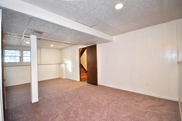 basement with a paneled ceiling and dark colored carpet