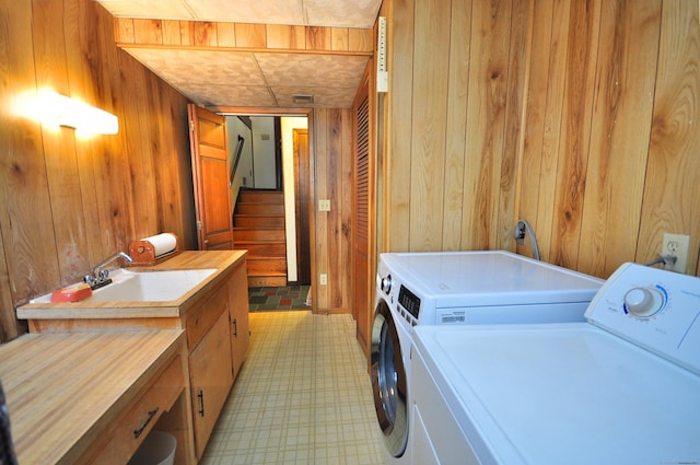 clothes washing area with cabinets, washing machine and dryer, sink, and wooden walls