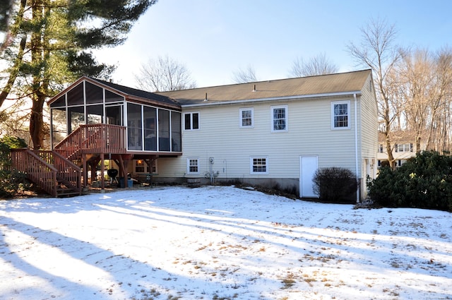 snow covered rear of property with a sunroom