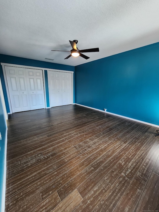 unfurnished bedroom featuring ceiling fan, two closets, a textured ceiling, and dark hardwood / wood-style flooring