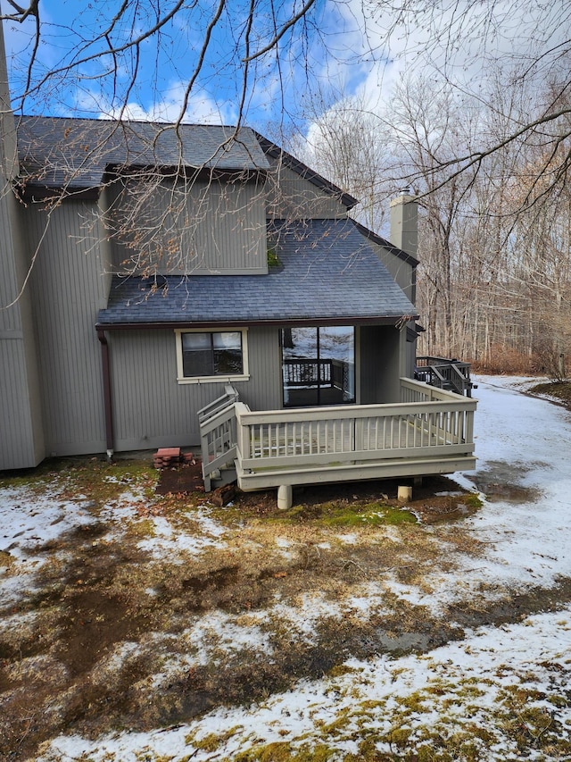 snow covered back of property with a wooden deck