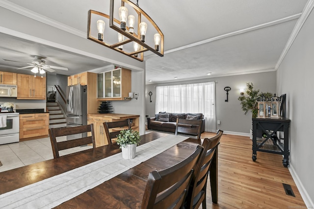 dining space with ceiling fan with notable chandelier, ornamental molding, and light hardwood / wood-style floors