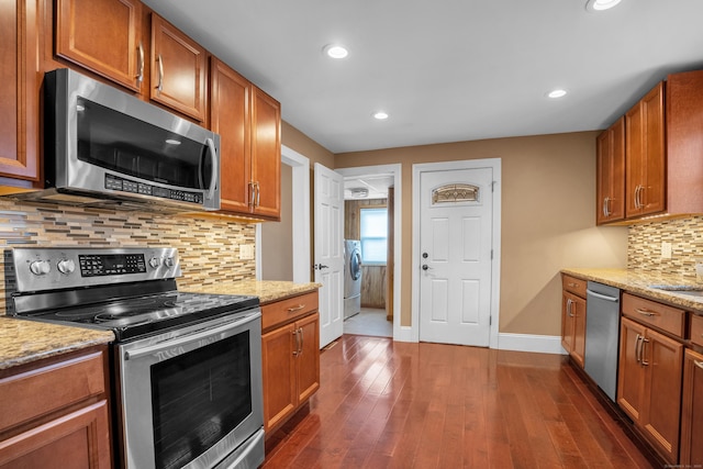 kitchen with stainless steel appliances, light stone countertops, dark hardwood / wood-style flooring, and washer / clothes dryer