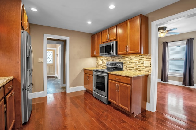 kitchen with backsplash, plenty of natural light, stainless steel appliances, light stone countertops, and dark hardwood / wood-style flooring