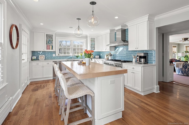 kitchen featuring white cabinetry, stove, a center island, and wall chimney range hood