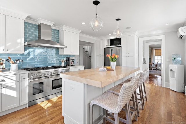 kitchen featuring wall chimney range hood, white cabinetry, a kitchen breakfast bar, a center island, and premium appliances