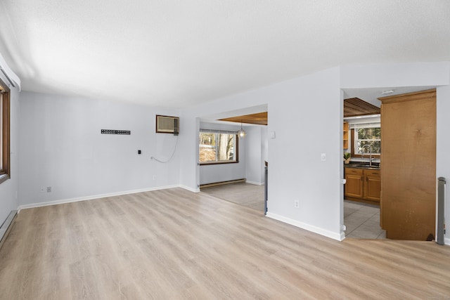 unfurnished living room featuring an AC wall unit, sink, light hardwood / wood-style floors, and a wealth of natural light