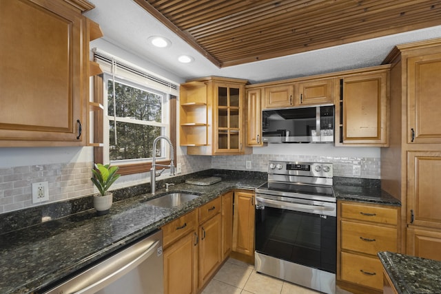 kitchen featuring sink, light tile patterned floors, dark stone countertops, appliances with stainless steel finishes, and backsplash