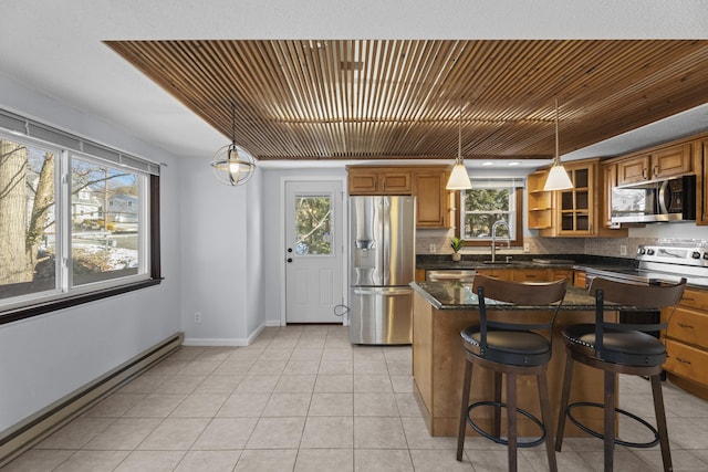 kitchen featuring pendant lighting, baseboard heating, appliances with stainless steel finishes, a center island, and a wealth of natural light