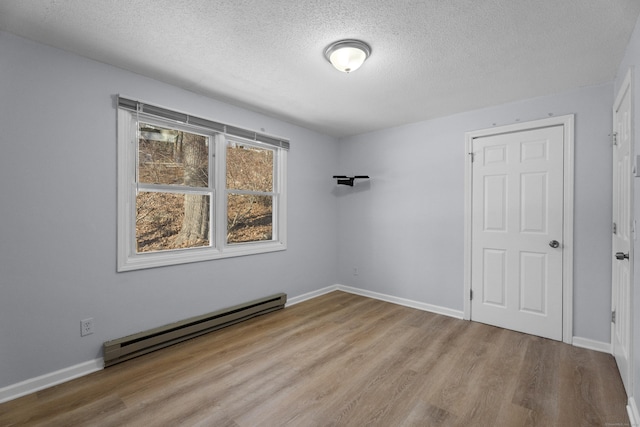 spare room with a textured ceiling, baseboard heating, and light hardwood / wood-style flooring