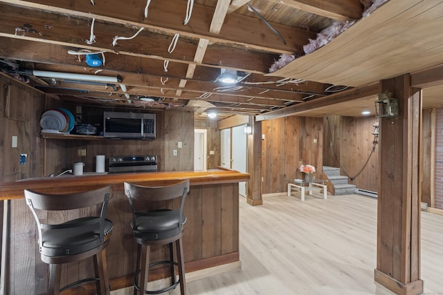 bar featuring stainless steel appliances, baseboard heating, wooden walls, and light hardwood / wood-style floors