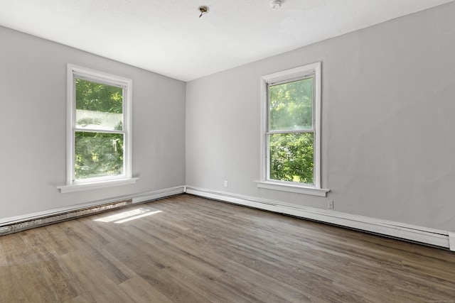 empty room with plenty of natural light, wood-type flooring, and baseboard heating