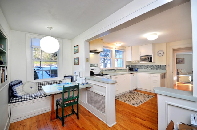 kitchen featuring pendant lighting, white range oven, stainless steel microwave, and white cabinets