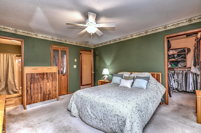 carpeted bedroom with ceiling fan, a spacious closet, a closet, and a textured ceiling