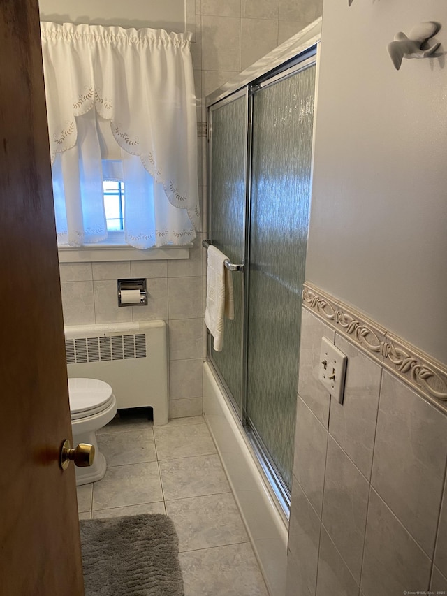 bathroom with shower / bath combination with glass door, tile walls, radiator heating unit, tile patterned floors, and toilet