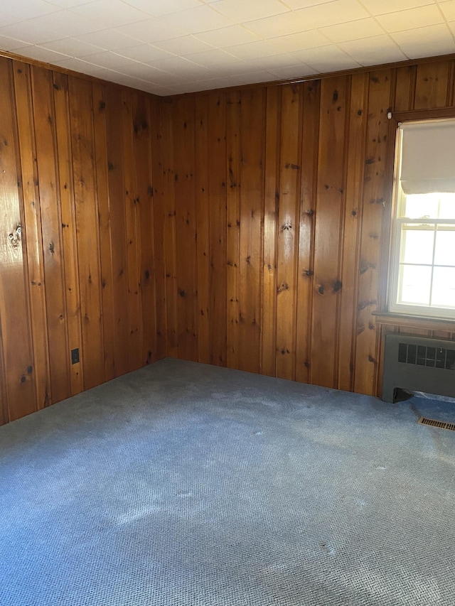 empty room with carpet flooring, radiator, and wood walls