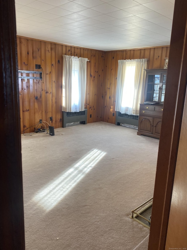 carpeted empty room featuring radiator and wooden walls