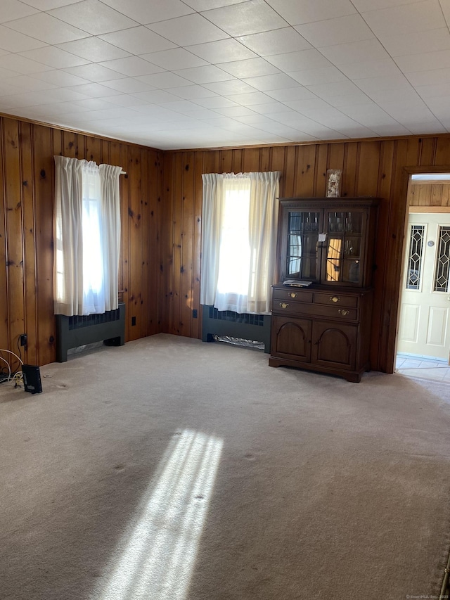 unfurnished living room with radiator, carpet floors, and wood walls