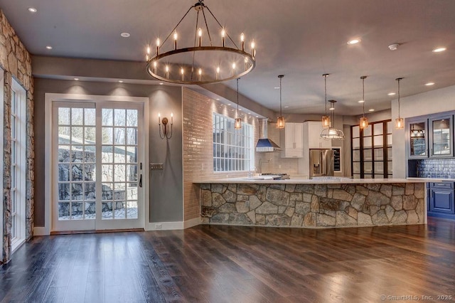 kitchen featuring wall chimney range hood, stainless steel fridge, dark wood-type flooring, hanging light fixtures, and backsplash