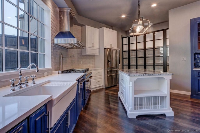 kitchen with pendant lighting, high quality appliances, blue cabinets, white cabinets, and wall chimney range hood