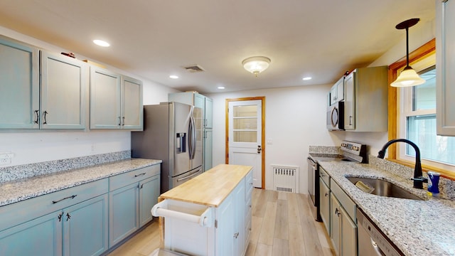 kitchen with pendant lighting, sink, light stone counters, light hardwood / wood-style floors, and stainless steel appliances