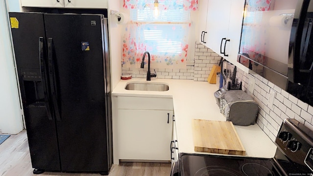 kitchen with sink, black fridge, tasteful backsplash, range with electric cooktop, and white cabinets