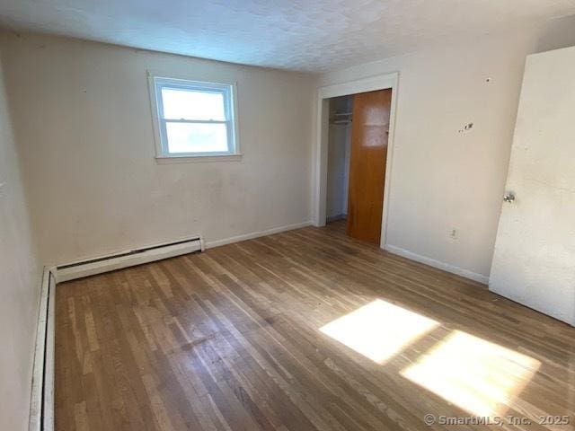 unfurnished bedroom featuring hardwood / wood-style floors, a closet, a textured ceiling, and baseboard heating