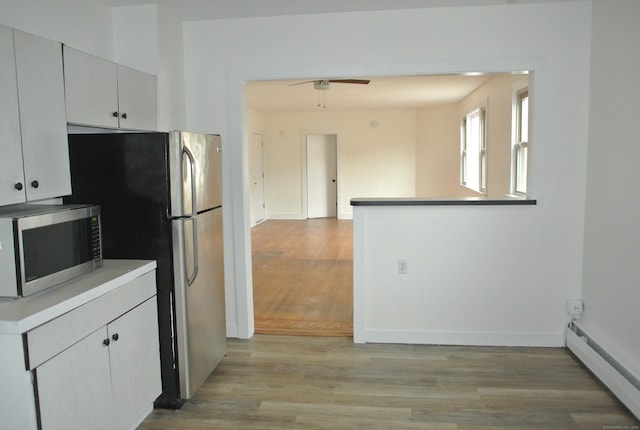 kitchen featuring ceiling fan, light wood-style flooring, a baseboard heating unit, white cabinetry, and appliances with stainless steel finishes