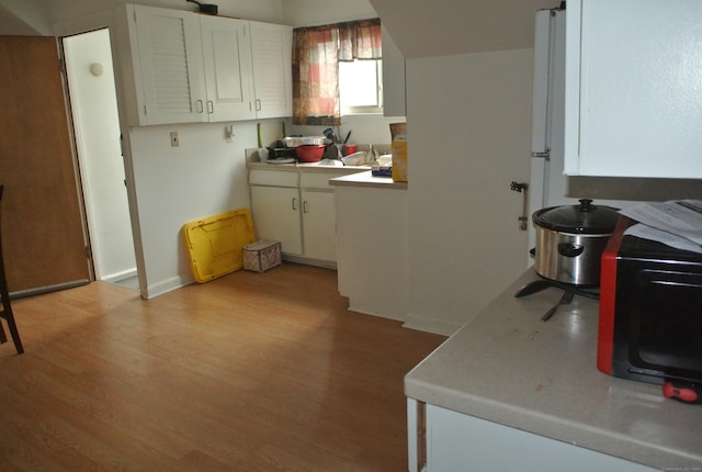 kitchen featuring light countertops, black microwave, white cabinetry, and light wood-style flooring