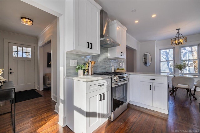 kitchen featuring wall chimney exhaust hood, stainless steel gas stove, ornamental molding, kitchen peninsula, and white cabinets