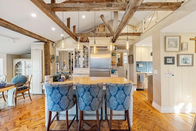 kitchen with a kitchen island, appliances with stainless steel finishes, glass insert cabinets, vaulted ceiling with beams, and a kitchen breakfast bar
