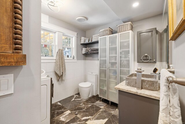 bathroom featuring toilet, vanity, wainscoting, washer / dryer, and marble finish floor