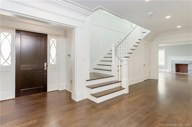 foyer featuring crown molding, dark wood-type flooring, and a fireplace