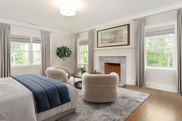 bedroom featuring hardwood / wood-style floors, crown molding, and a premium fireplace