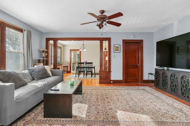 living room with ceiling fan, decorative columns, baseboards, and wood finished floors