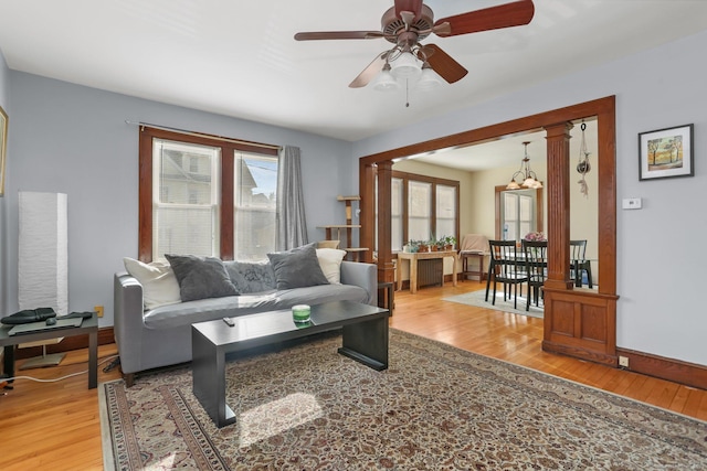 living room with ornate columns, a ceiling fan, baseboards, and light wood-style floors