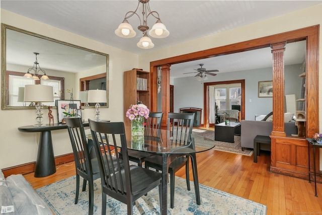 dining space with ceiling fan with notable chandelier, light wood finished floors, and ornate columns