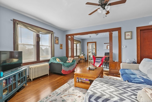 living room featuring a ceiling fan, light wood-type flooring, ornate columns, and radiator heating unit