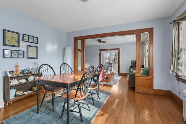 dining space featuring ornate columns, a ceiling fan, baseboards, and wood finished floors