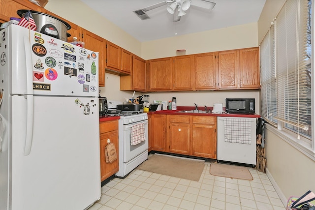 kitchen with brown cabinets, dark countertops, a sink, ceiling fan, and white appliances