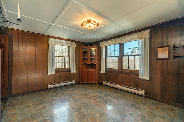 spare room with a healthy amount of sunlight, visible vents, a baseboard heating unit, and wooden walls