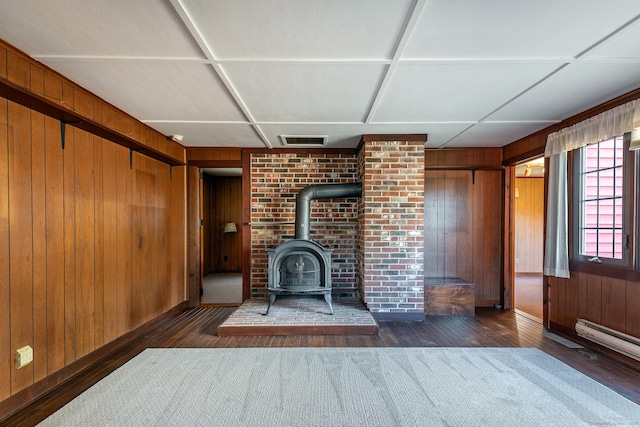 unfurnished living room with wood finished floors, wood walls, a wood stove, baseboards, and visible vents
