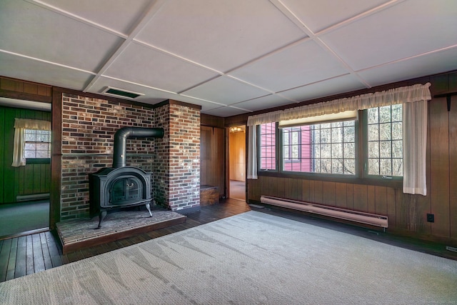 unfurnished living room with a baseboard radiator, visible vents, wood walls, and a wood stove