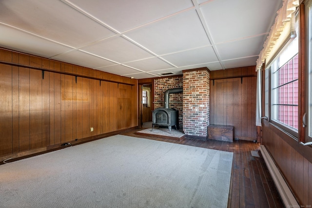 unfurnished living room featuring dark wood-style flooring, wood walls, a wood stove, and baseboard heating
