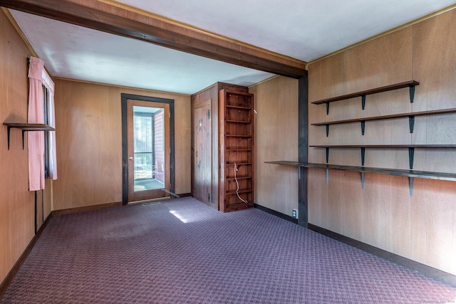 spare room featuring beam ceiling, wooden walls, dark colored carpet, baseboards, and visible vents